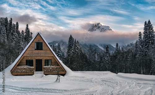 Wooden house at mountain peak and clouds background. Panoramic view of winter landscape at sunset time. Anchkho mount in Abkhazia