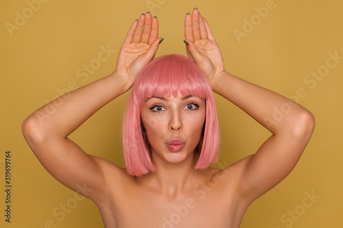 Obraz na plátne Studio shot of charming young blue-eyed lady with pink bob hairstyle putting her