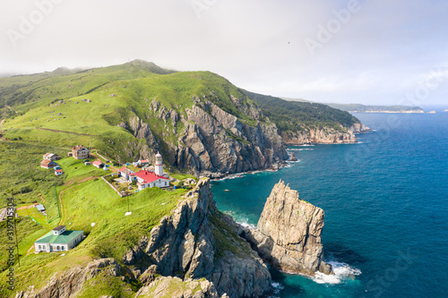 Gamov Lighthouse on steep cliff of rocky sea coastline. Aerial view of Cape Gamov at Gamov Peninsula in sunny summer weather. Seaside nature landscape in Primorsky Krai, Far East, Russia photo