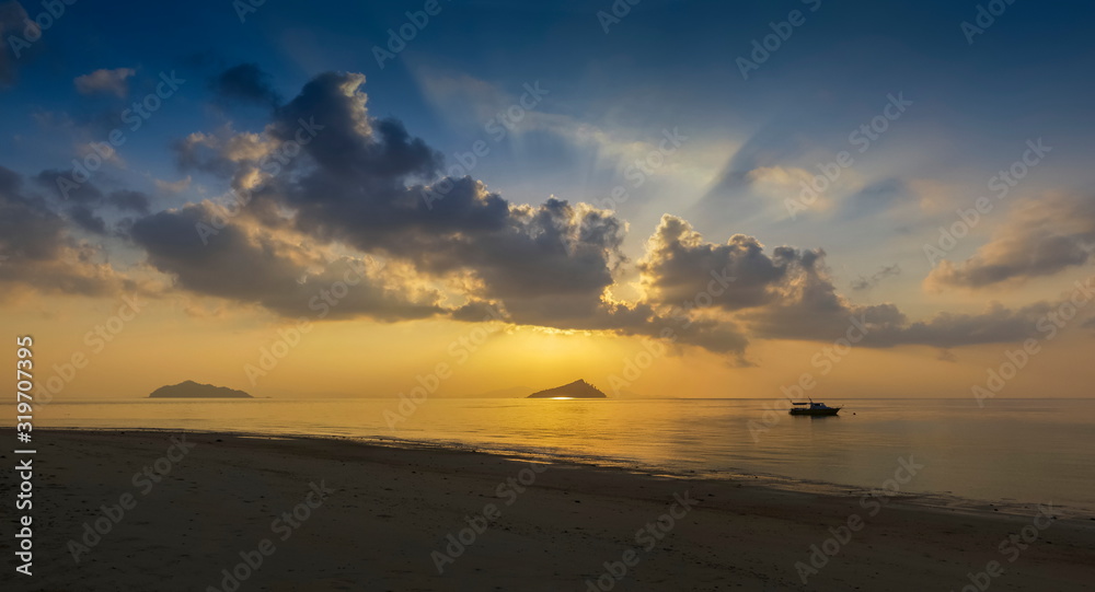 Obraz premium view panorama seaside of small boat floating in the sea with small island and sun rays with yellow sun light and cloudy sky background, sunrise at Ko Bulon Le, Stun Province, southern of Thailand.