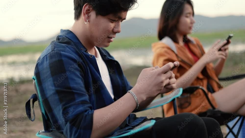 Close up hands asian man using smartphone playing games with a girlfriend sitting beside a tent camping. Trekking, camping trip on vacation summer. Close up hands asian man using smartphone playing games with a girlfriend sitting beside a tent camping. Trekking, camping trip on vacation summer.