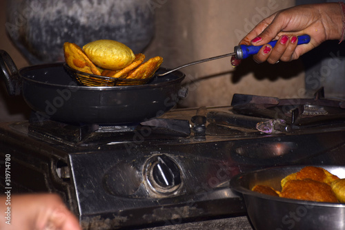 hands of a woman frying poodi on LPG gas stove, boiling oil in frying pan with dark background photo