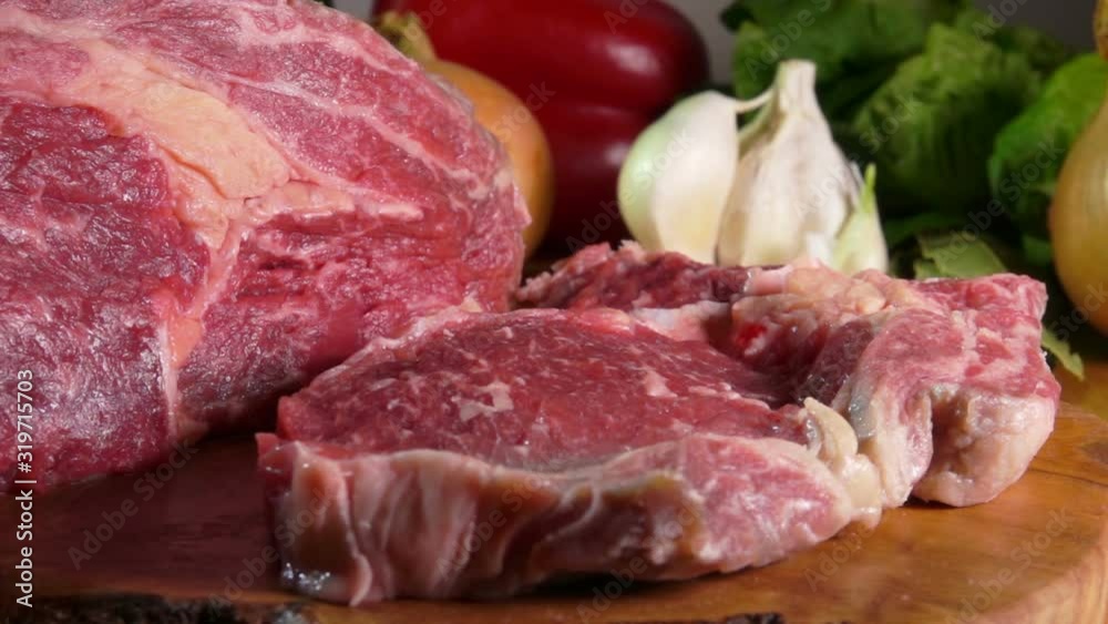 Raw meat steak falls on the wooden board on the background of vegetables Raw meat steak falls on the wooden board on the background of vegetables