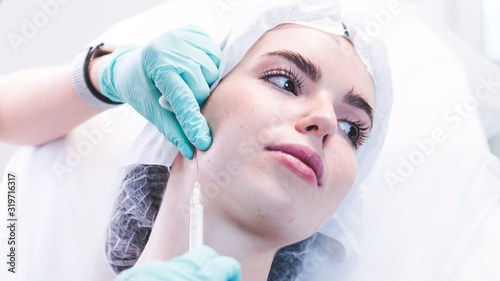 The female beautician doctor making injection in young woman face. The doctor cosmetologist doing facial contouring procedure.