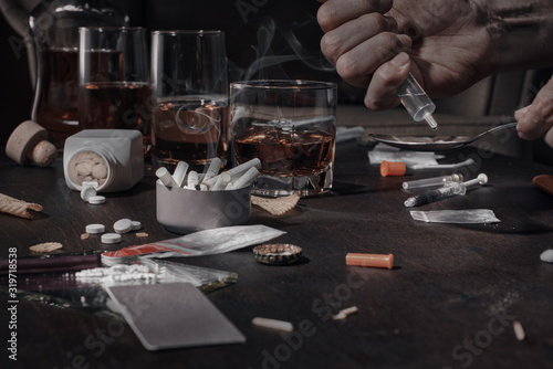 Various drugs, alcohol and cigarettes are on the wooden table. Substances that cause drug and alcohol dependence. Low key.