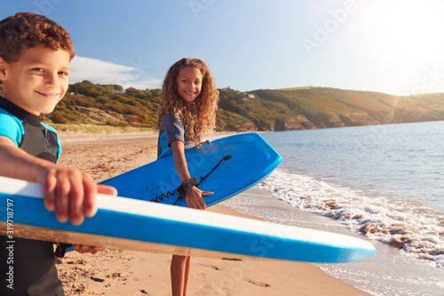 Photos Portrait Of Children Wearing Wetsuits Carrying Bodyboards On Summer Beach Vacati