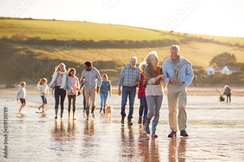 Active Multi-Generation Family With Dog Walking Along Shore On Winter Beach Vacation