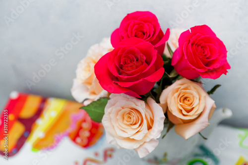 Romantic bouquet of red and creme beige roses as gift to st. Valentine holiday on colorful table and gray background