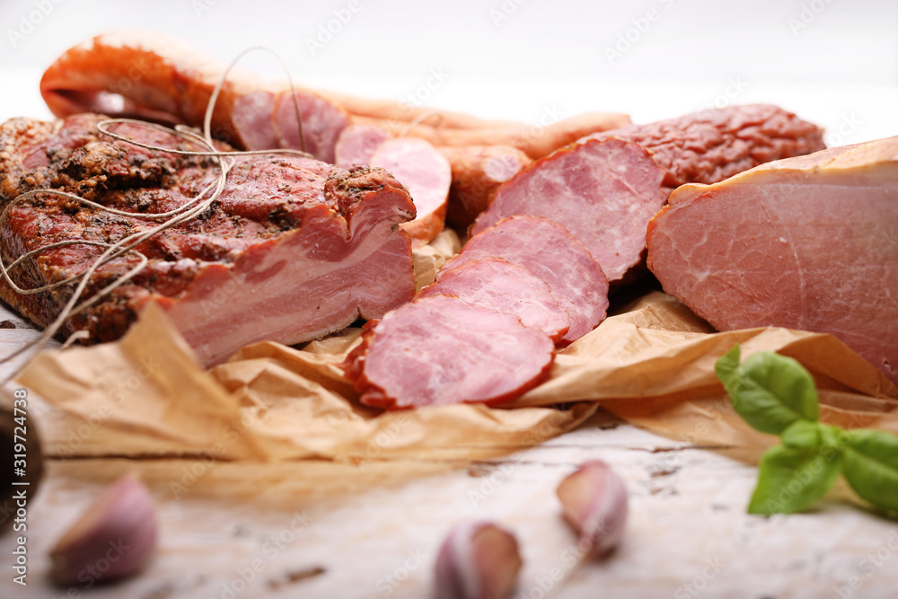 Smoked cold cuts on a paper and wooden boards with garlic and herbs. Traditional meat products.