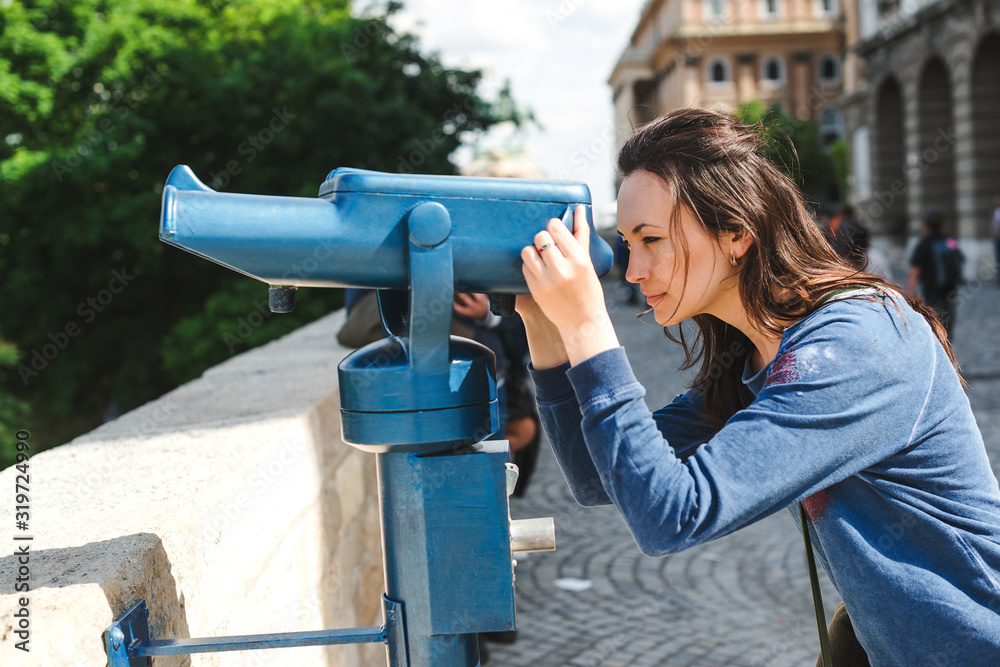 Woman watching on city panorama in the observation binoculars. Summer vacations.