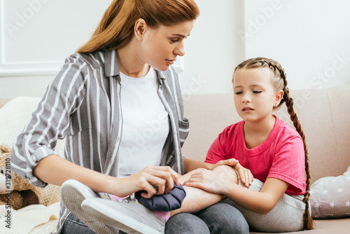 mother holding ice bag compress on painful knee of emotional daughter