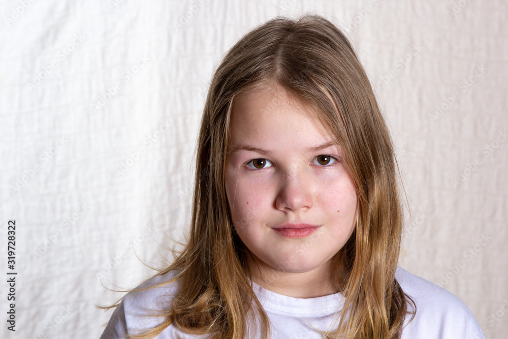 Portrait of blond beautiful girl 10 years old in front on light background, looking at camera, closeup Portrait of blond beautiful girl 10 years old in front on light background, looking at camera, closeup