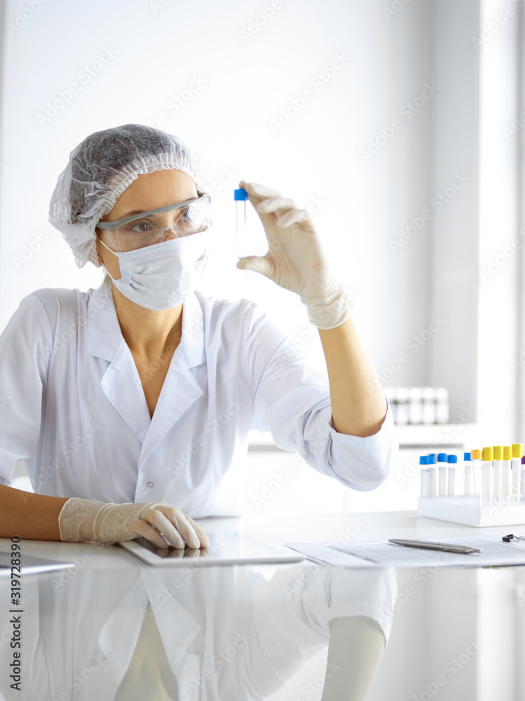 Naklejka premium Professional female scientist in protective eyeglasses researching tube with reagents in laboratory. Concepts of medicine and research