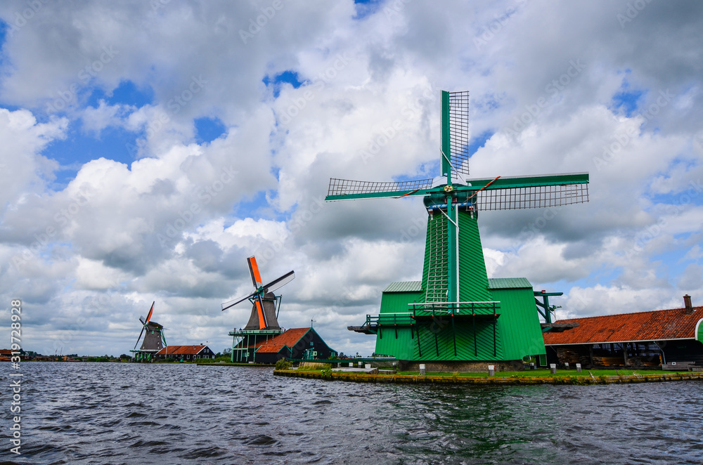 Zaanse Schans, Holland, August 2019. Northeast Amsterdam is a small community located on the Zaan River. View of the mills on the river bank, they stand out with their bright colors. Cloudy day.