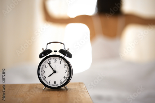 Woman stretching hands in bed after wake up, sun flare . Brunette entering a day happy and relaxed after good night sleep and back view. Concept of a new day and joyful weekend