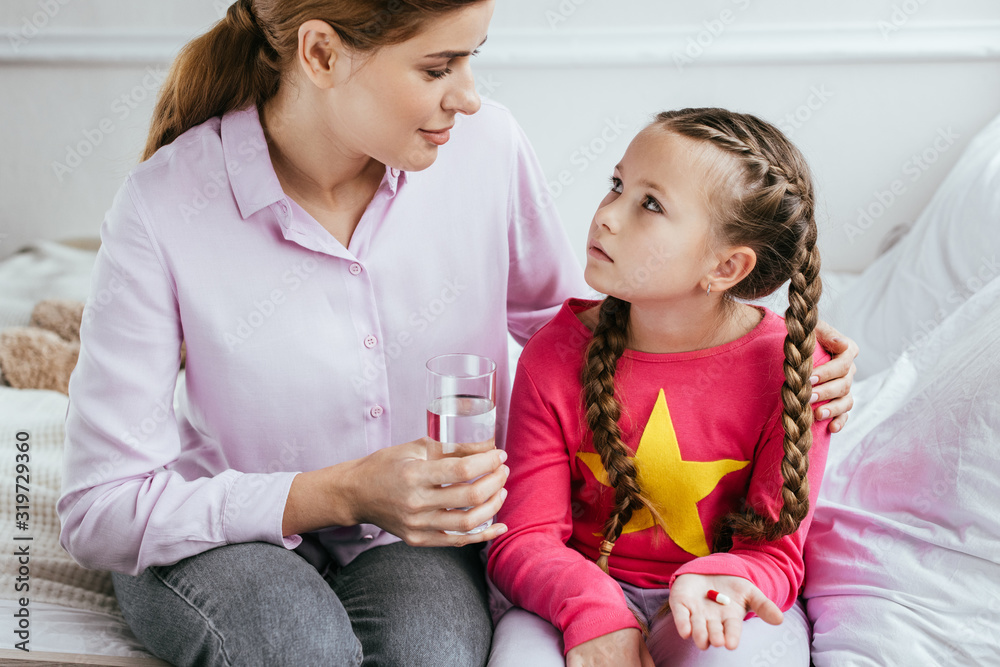 smiling mother giving glass of water to diseased daughter with pill smiling mother giving glass of water to diseased daughter with pill