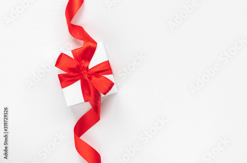 White gift box with red ribbon on white background. Top view. Holiday time at any time of the year