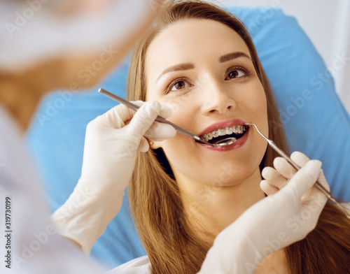 Smiling young woman with orthodontic brackets examined by dentist at dental clinic. Healthy teeth and medicine concept