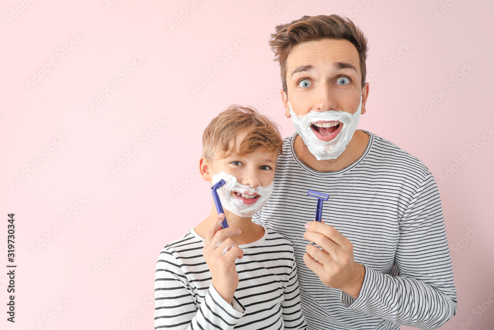 Funny father and his little son shaving against color background