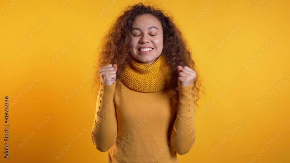 Girl with curly hair very glad and happy, she shows yes gesture of victory, she achieved result, goals. Surprised excited happy woman on yellow background Girl with curly hair very glad and happy, she shows yes gesture of victory, she achieved result, goals. Surprised excited happy woman on yellow background