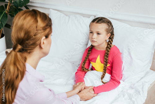 attractive mother holding hands with ill daughter in bed