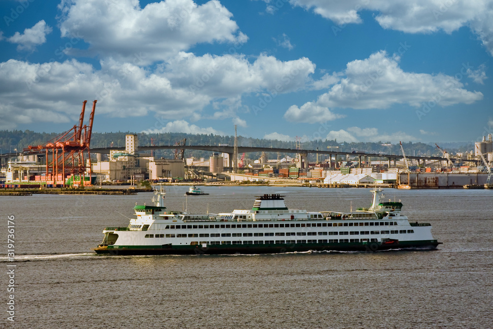 A large ferry crossing the bay past a shipping and freight yard