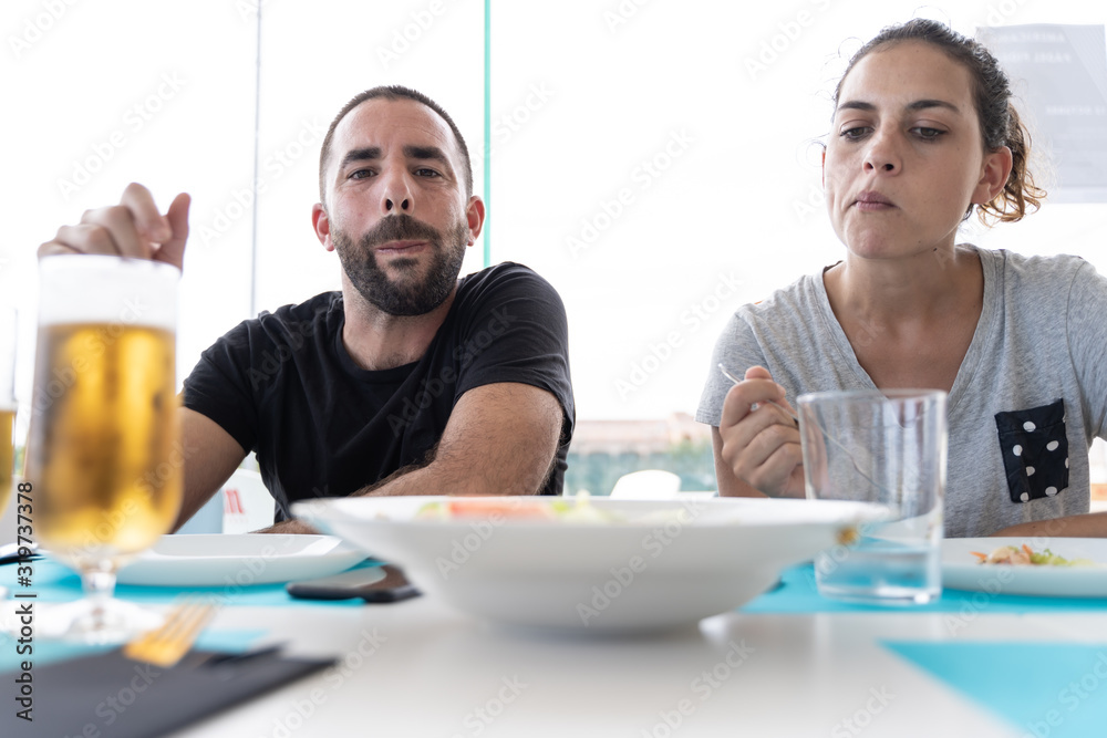 Couple looking at the plate of food in the middle of the table with a fork in hand ready to take salad from a shared plate