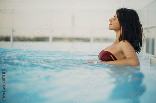 Beautiful young woman relaxing in pool hot tub, smiling and enjoying day. Happy brunette girl on summer vacation in luxury resort, swimming in pool on rooftop with view on sea. Copy space