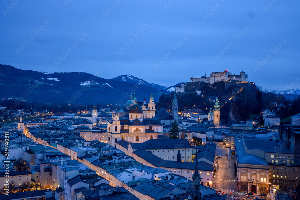 Salzburg evening cityscape with main Cathedral, Kollegienkirche and illuminated streets of old town on background of mountains in clouds