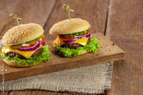 Meal, food. Two hamburger with cutlet grilled, lettuce, tomato, cheese, cucumber on a light wooden background.