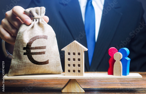 Man puts euro money bag and house on scales with a family. Mortgage, debt burden. Assistance with housing, financing young families to stimulate childbirth demographic population growth. Social help