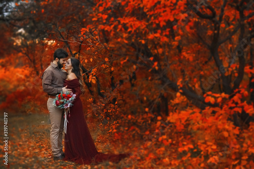 In the autumn of a woman with a man embracing in the Park with red trees.