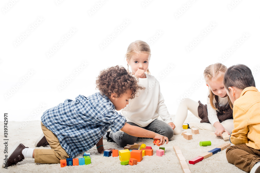 Obraz premium multicultural kids playing with wooden blocks on carpet, isolated on white