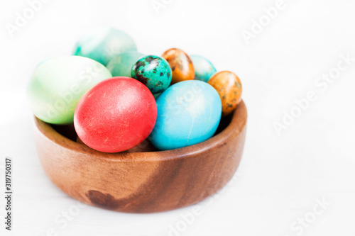 Easter background. Bright multi-colored Easter eggs in a wooden plate on a white wooden surface, close-up