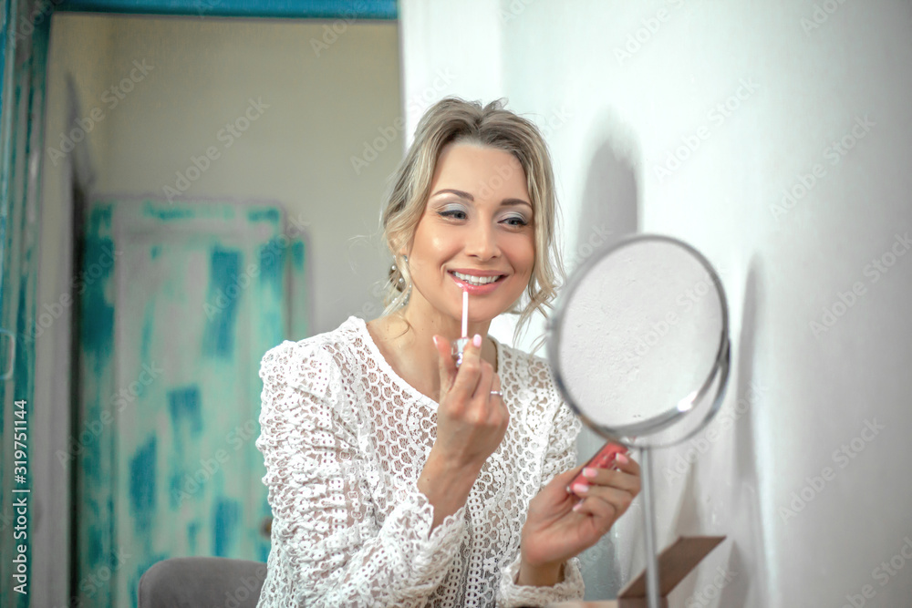 Female portrait of beautiful wedding make-up and hairstyle. The face of woman is posing , model paints lips with lipstick, look to the mirror. The morning of bride dressed white openwork dress Female portrait of beautiful wedding make-up and hairstyle. The face of woman is posing , model paints lips with lipstick, look to the mirror. The morning of bride dressed white openwork dress