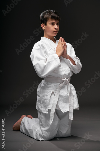 sport concept - greeting bow, a teenager dressed in martial arts clothing poses on a dark gray background, studio shoot