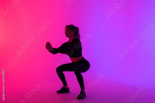 Full length portrait of a young fitness woman doing squatting isolated on a vibrant colors background