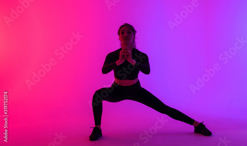 Full length portrait of a young fitness woman doing squatting isolated on a vibrant colors background