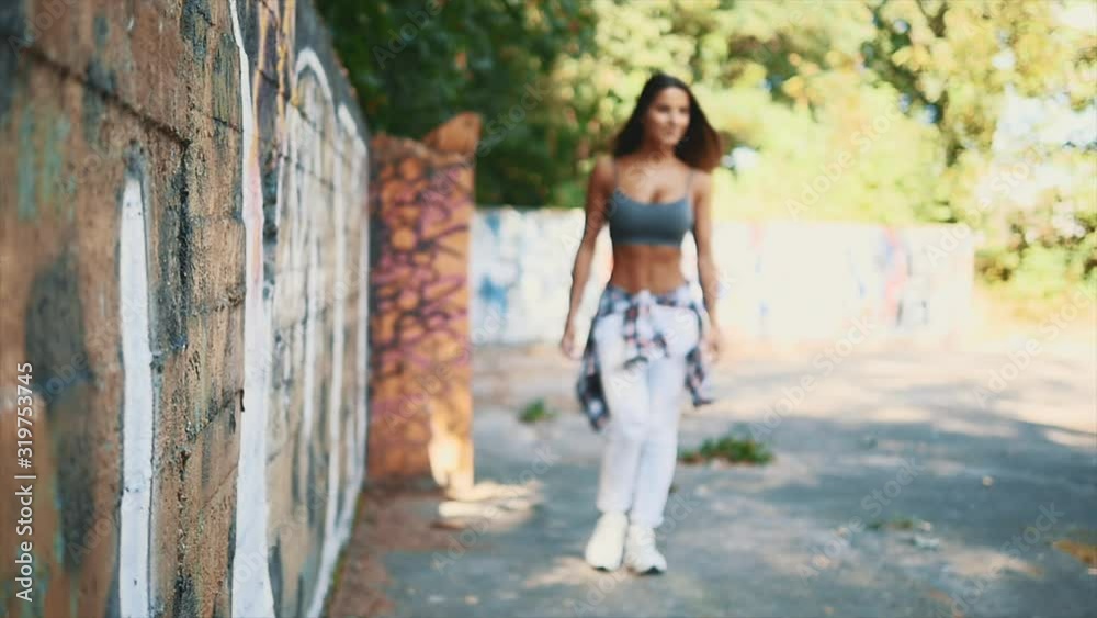 Sexy and sportish girl is walking along the graffiti wall. Copy space. Slowmo. Slow motion. 4K. Sexy and sportish girl is walking along the graffiti wall. Copy space. Slowmo. Slow motion. 4K.