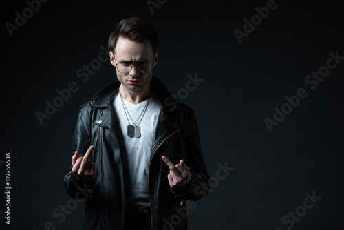 stylish brutal man in biker jacket showing middle fingers isolated on black