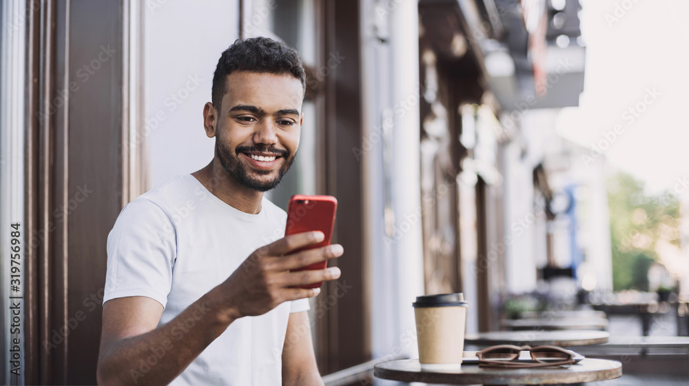 Handsome man using smartphone in a city. Young handsome student men having coffee break and texting on his mobile phone. Modern lifestyle, city life concept Handsome man using smartphone in a city. Young handsome student men having coffee break and texting on his mobile phone. Modern lifestyle, city life concept
