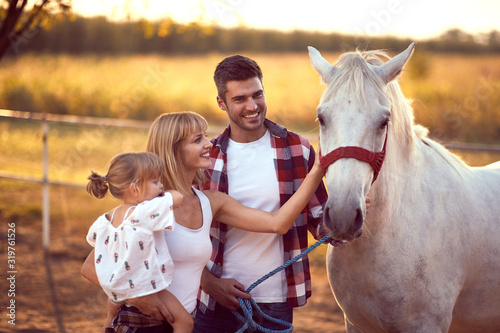 Happy family petting a white horse. Fun on countryside, sunset golden hour. Freedom nature concept.