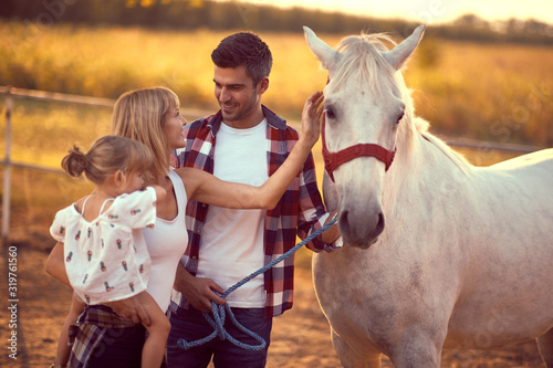 Family of three bonding with a white horse. Fun on countryside, sunset golden hour. Freedom nature concept.