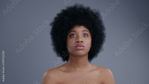 Portrait of beautiful serious african girl interacting with hologram on grey background. Close-up of topless attractive afro-american girl with curly hair using a future touchscreen.