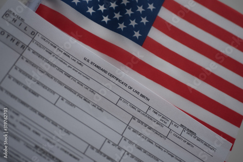 U.S. standard certificate of live birth application form next to flags of USA. Birthright citizenship concept. Diagonal view.