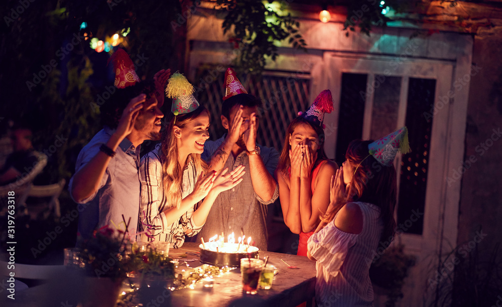 Foto Stock Smiling group of young friends having birthday party in the club  with cake and candles at night. Party, fun, birthday concept. | Adobe Stock