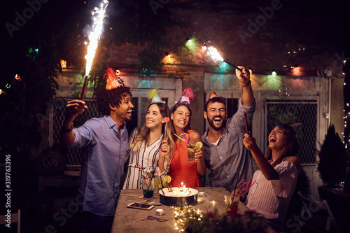 Smiling group of young friends having  birthday party in the club with cake and candles at night.  Party, fun, birthday concept.