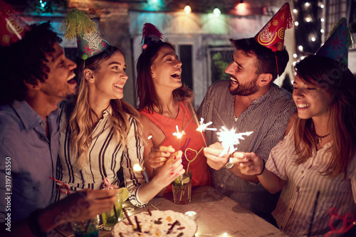 Foto Smiling group of young friends having  birthday party in the club with cake and candles at night