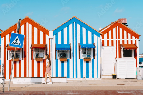 small traditional and colorful houses of costa nova. young beautiful woman walking along street with typical striped houses in Costa Nova, Aveiro, Portugal. Fisherman's village in summer.