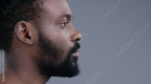 Profile of attractive topless emotionless afro-american young man standing straight looking forward isolated on dark background.